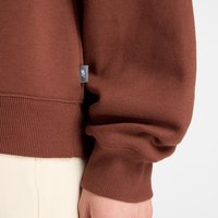 Sweatshirt castanho com punhos e bainha canelados, uma pequena etiqueta lateral e uma textura suave. As mangas têm um ajuste ligeiramente descontraído.