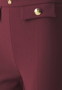 Bordo hlače s glatkom tkaninom, jednostavnim dizajnom, vertikalnim šavovima i zlatnim dugmadima kao detaljima za kopčanje.