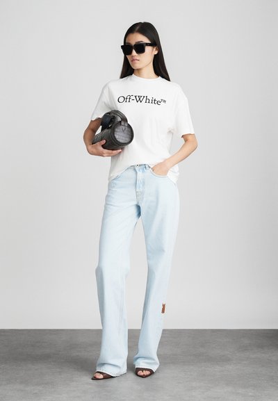 Naine kannab musti päikesegelasse, valget Off-White t-särki, helesiniseid avaraid pükse, pruune avatud varvastega kingi ning hoiab käes musta tekstuuriga käekotti.