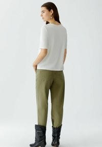 Weißes kurzärmliges Oberteil, kombiniert mit olivgrünen Hosen und schwarzen kniehohen Stiefeln, das ein einfaches Design und eine glatte Stofftextur zeigt.