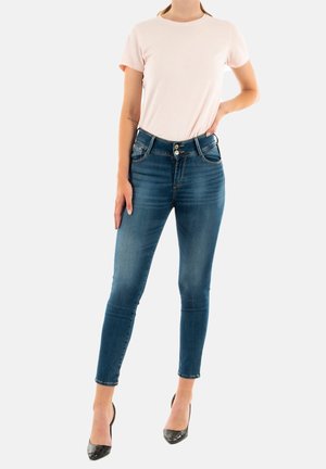 T-shirt rose clair à manches courtes associé à un jean skinny en denim bleu foncé avec cinq poches et une fermeture à bouton, porté avec des talons noirs.
