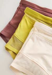 Trois sous-vêtements féminins pliés en marron, jaune et beige avec des panneaux en tissu mesh sur une surface claire.