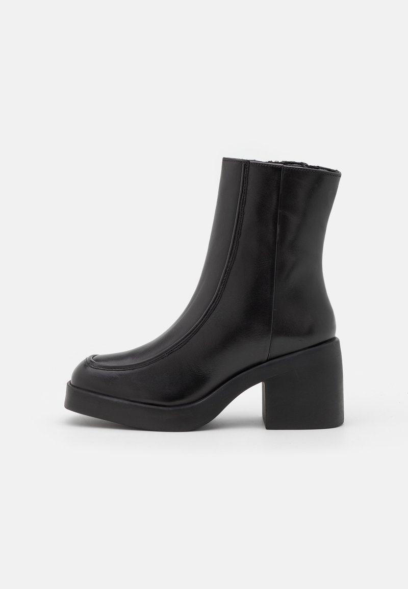 Bottine en cuir noir à bout arrondi, fermeture éclair latérale et talon bloc épais sur un fond clair uni.