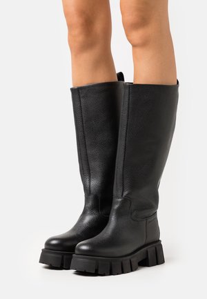 Black leather knee-high boots feature a textured finish, chunky rubber sole, and minimalistic design with no visible hardware or accents.