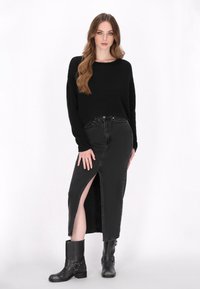 Pull en maille noir, jupe en denim noir taille haute avec une fente sur le côté, portée avec des bottes noires mi-mollet avec un détail de sangle.
