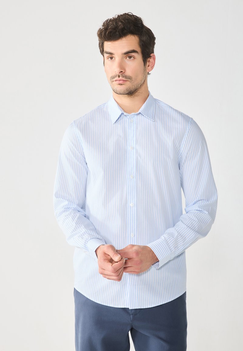 Camisa de botones de manga larga azul claro con rayas blancas verticales, cuello clásico y dobladillo redondeado. El tejido parece suave y ligero.