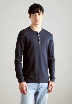 Marinblå långärmad henley-tröja i mjukt tyg, med rund krage och femknäppt knappslå, bärs med ljusblå jeans.