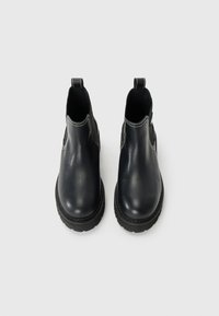 Bottines en cuir noir avec des panneaux élastiques sur les côtés et des tirants, ornées de coutures blanches et dotées de semelles en caoutchouc épaisses pour une meilleure adhérence.