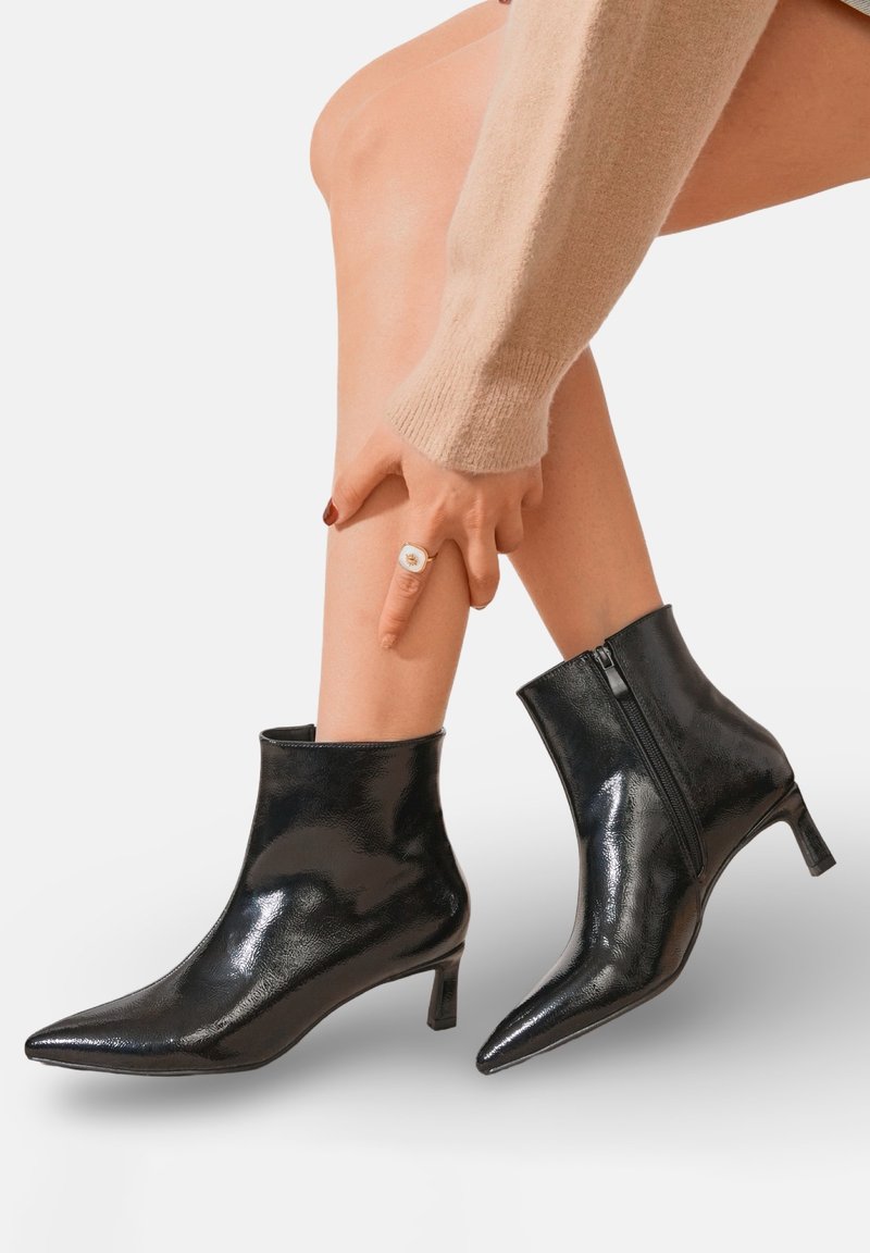 Bottines noires en cuir brillant, avec un bout pointu, un petit talon et une fermeture éclair sur le côté.