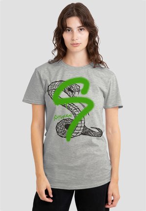 Young woman with shoulder-length brown hair wears gray t-shirt featuring coiled snake and large green "S" with text "Slytherin."