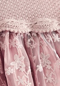 Pinker Stoff mit gehäkeltem Oberteil und mehrlagigem floralen Spitzen-Tüllrock, der Struktur und detaillierte florale Stickereimuster zeigt.