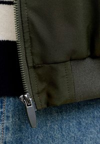 Grønt bomberjakke stof med en blød finish, udstyret med lynlåslukning foran, ribstrikkede ærmekanter og en kontrasterende inderfor.