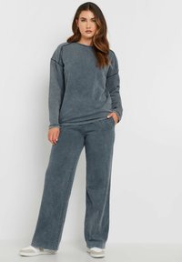 Grå sweatshirt och matchande vida byxor i ett mjukt, tvättat tyg. Har rundad halsringning och detaljer i sidsömmen. Vita sneakers fulländar looken.