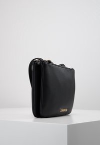 Czarna skórzana torebka o eleganckim prostokątnym kształcie, z podwójnym zamkiem błyskawicznym i złotym logo na dolnej przedniej części. Gładka faktura.