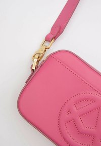 Borsa a tracolla in pelle rosa con accessori dorati, caratterizzata da un logo in rilievo prominente, texture liscia e tracolla regolabile.