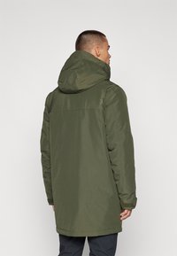Grön vattentät parka med huva, som har en rak skärning, långa ärmar och elastiska muddar. Bakåtsidan visar en jämn textur och minimala detaljer.
