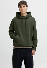 Olive green hoodie made of soft fabric with a front pocket, drawstring hood, and ribbed cuffs, worn over a gray shirt and dark pants.