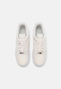Paire de baskets basses blanches avec une pointe perforée, des lacets blancs et un col rembourré, vues de dessus sur un fond gris.
