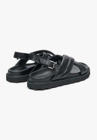Černé kožené sandály s širokými křížovými pásky, nastavitelným páskem kolem kotníku a silnou, texturovanou černou gumovou podrážkou. Celkově elegantní design.