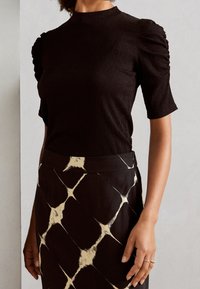 Černý proužkovaný top s krátkými nabíranými rukávy a vysokým límcem, kombinovaný s patterned sukní s designem diamantů v krémové a černé barvě.