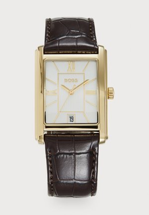 Montre rectangulaire dorée avec cadran blanc, chiffres romains et affichage de la date ; bracelet en cuir texturé marron avec motif crocodile.