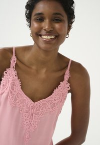 Roza brezrokavnik z zapletenim čipkastim okrasom okoli ovratnika, s tankimi naramnicami in gladko, lahko teksturo tkanine.