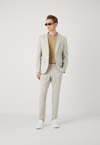 Svijetlo sivi odijelo, bež majica i bijele tenisice. Slim fit dizajn, glatka tekstura i minimalni detalji na odijelu i majici.