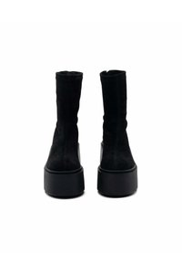 Stivali alla caviglia in suede nero con una suola piatta e rugged. Il design presenta una silhouette elegante e aderente con una finitura liscia.