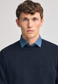 Felpa blu navy con "POLO CLUB" in rilievo sul davanti, abbinata a un colletto in denim azzurro. Tessuto morbido e design classico.