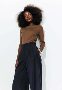 Haut marron à manches longues associé à un pantalon large à rayures bleues marines taille haute. Un bracelet au poignet ajoute une touche subtile.