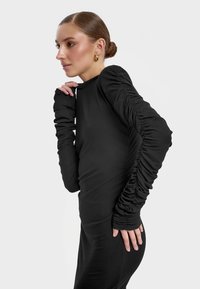 Czarna sukienka z długim rękawem, z marszczonymi detalami na rękawach, dopasowana sylwetka i gładka faktura. Prosty okrągły dekolt i brak wzorów.