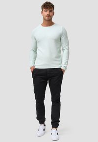 Lys grønne ribbede langærmede sweater i kombination med sorte joggerbukser og hvide sneakers. Simpelt design med en tætsiddende silhuet og manchetter ved anklerne.