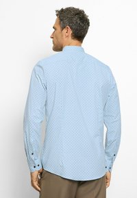 Helles Blau langärmliges Hemd mit gepunktetem Muster, kontrastierenden schwarzen Knöpfen und abgerundetem Saum. Der Stoff wirkt glatt mit einer taillierten Passform.