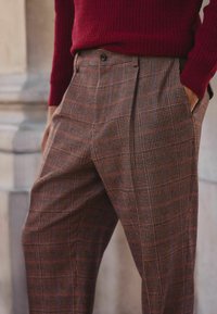 Check pattern trousers in brown, red, and cream tones. Made of textured fabric with a relaxed fit and side pockets. Designed with front pleats.