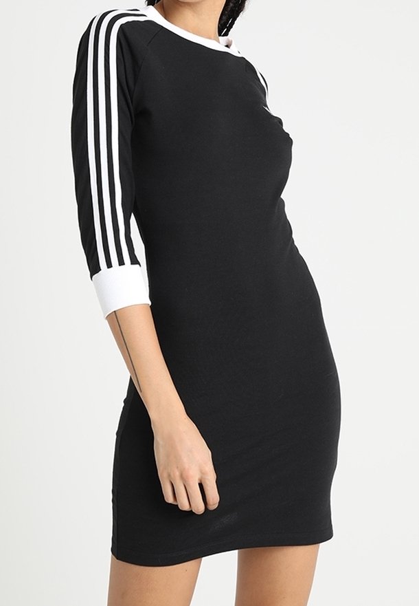 Robe noire avec des manches trois quarts, col blanc, et rayures blanches sur les manches. Fabriquée dans un tissu lisse, coupe bodycon, longueur genoux.