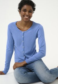 Blauwe gebreide cardigan met een ronde halslijn, knopen aan de voorkant en geribde mouwringen. Zachte textuur, gedragen over vervaagde blauwe jeans.