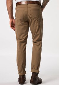 Khaki-Chinos mit geradem Bein, rückseitige Taschen mit dezenten Nähten, umgeschlagenen Säumen und sichtbaren abgenutzten braunen Lederstiefeln.