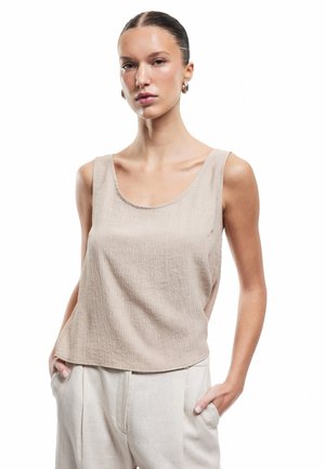 Beige tekstureret tanktop med rund hals og brede skulderstropper, parret med lyse beige bukser. Glat stof med subtile variationer.