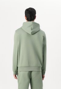 Sudadera con capucha de tejido verde claro con una textura suave. Incluye puños y dobladillo de canalé, mostrada por la parte de atrás con pantalones a juego.