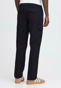Black cargo pants with a straight fit, featuring side pockets, back pockets, and a textured fabric. Worn with gray sneakers.