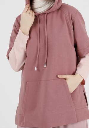 Hoodie côtelé rose avec poche kangourou, cordons de serrage avec embouts en métal, et manches courtes, superposé à un haut à manches longues rose clair.