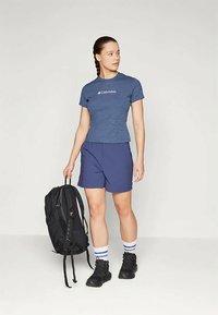 Blue athletic t-shirt with Columbia logo, navy shorts, striped ankle socks, and black backpack; standing pose on light background.