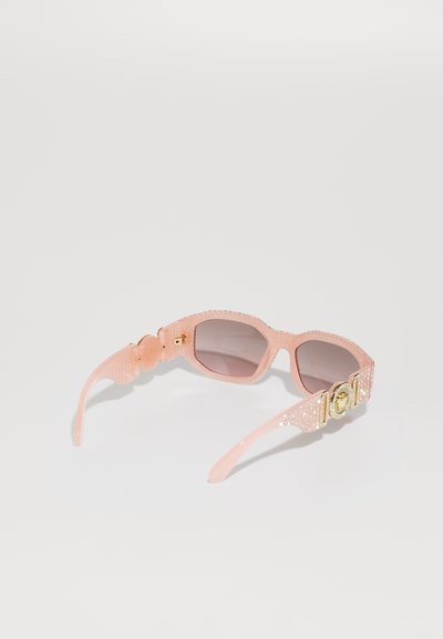 Óculos de sol rosa com uma armação texturizada, lentes degradê e detalhes em ouro acentuados com strass nas hastes. Forma quadrada.