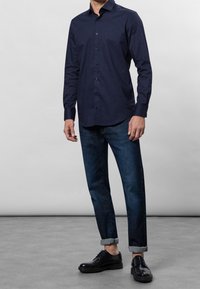 Marinblå skjorta med knappar, i bomullstyg, långa ärmar. Matchad med mörka jeans med uppvikta ärmslut och svarta snörskor med polerad yta.