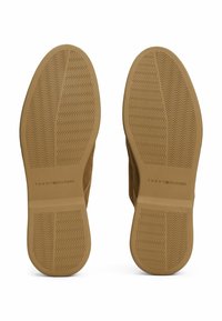 Schoenen met een bovenwerk van bruin suède en een gestructureerde rubberen zool. De zool heeft een golfpatroon en een gedrukt logo: "TOMMY HILFIGER."