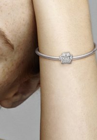 Bracciale d'argento con un design intrecciato. Presenta un charm a forma di zampa decorato con piccole pietre scintillanti al centro.