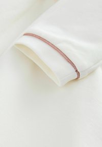Weißer Stoff mit glatter Textur, der an der Naht mit einem gefalteten Bund versehen ist, akzentuiert durch einen metallischen roségoldenen Faden.