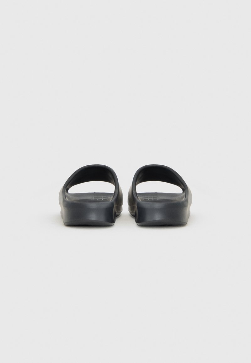 Tongs en caoutchouc noir avec un dos et des côtés ouverts, présentant une texture lisse et une forme légèrement courbée. Design minimaliste.