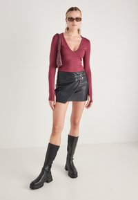 Bordová dlhá rukávová body, čierna sukňa z imitácie kože s detailom dvojitého pracky, čierne vysoké platformové čižmy po kolená a slnečné okuliare.