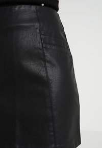 Černá sukně z umělé kůže s texturovaným povrchem, detailním prošitím a boční kapsou. Střih je přiléhavý a mírně rozšířený.